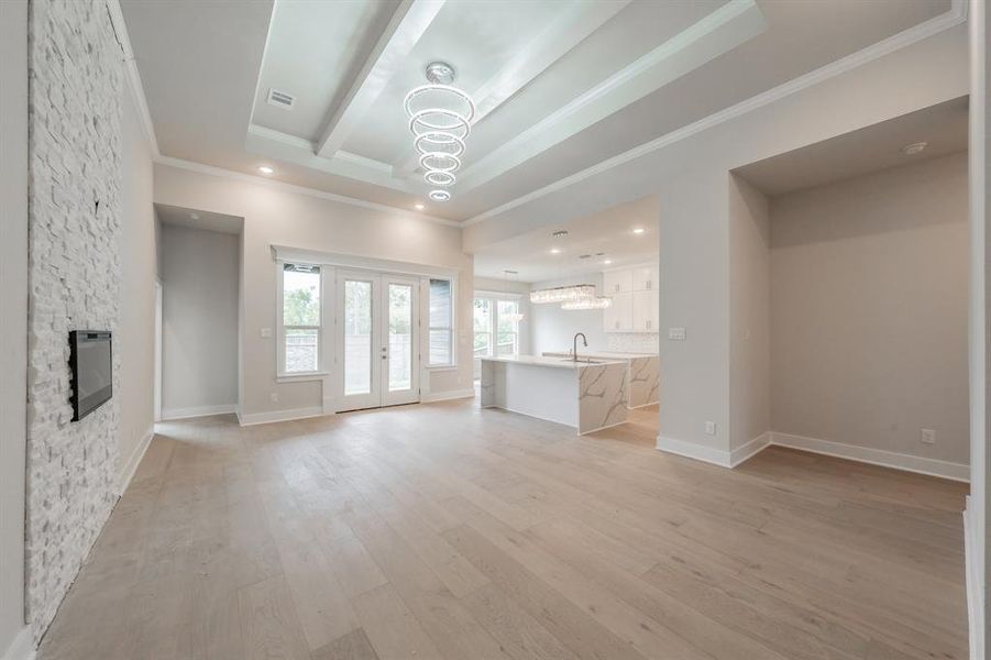 Unfurnished living room with ornamental molding, light wood-style flooring, a chandelier, french doors, and a fireplace