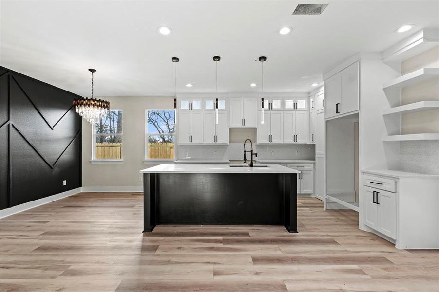 Kitchen with pendant lighting, white cabinetry, a notable chandelier, and an island with sink