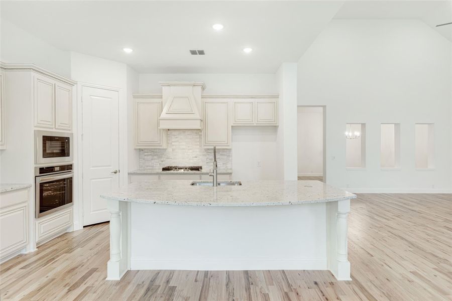 White kitchen with large curved island, granite countertops, stainless steel appliances, and light hardwood floors