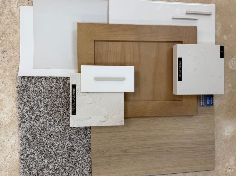 Home design material samples including white cabinet doors, wood flooring, quartz countertop swatches, and gray carpet sample.