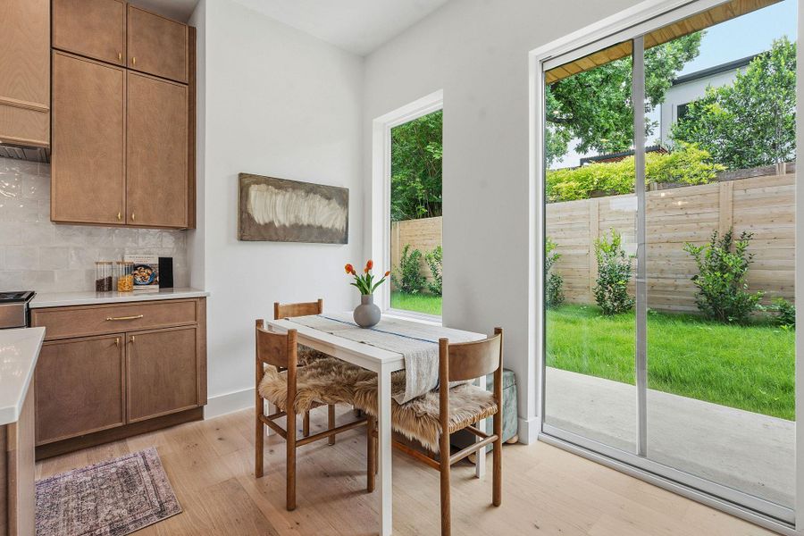 Kitchen dining area featuring wood-finish cabinetry with brass hardware, a white countertop, and a light-toned tile backsplash