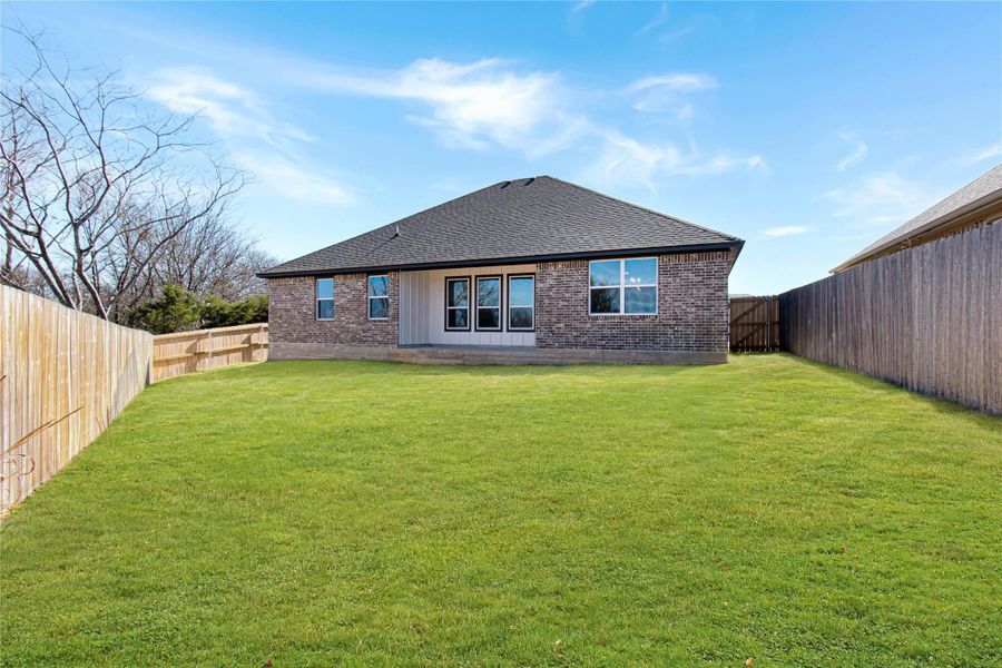 Back of house with brick siding, a fenced backyard, a shingled roof, and a patio