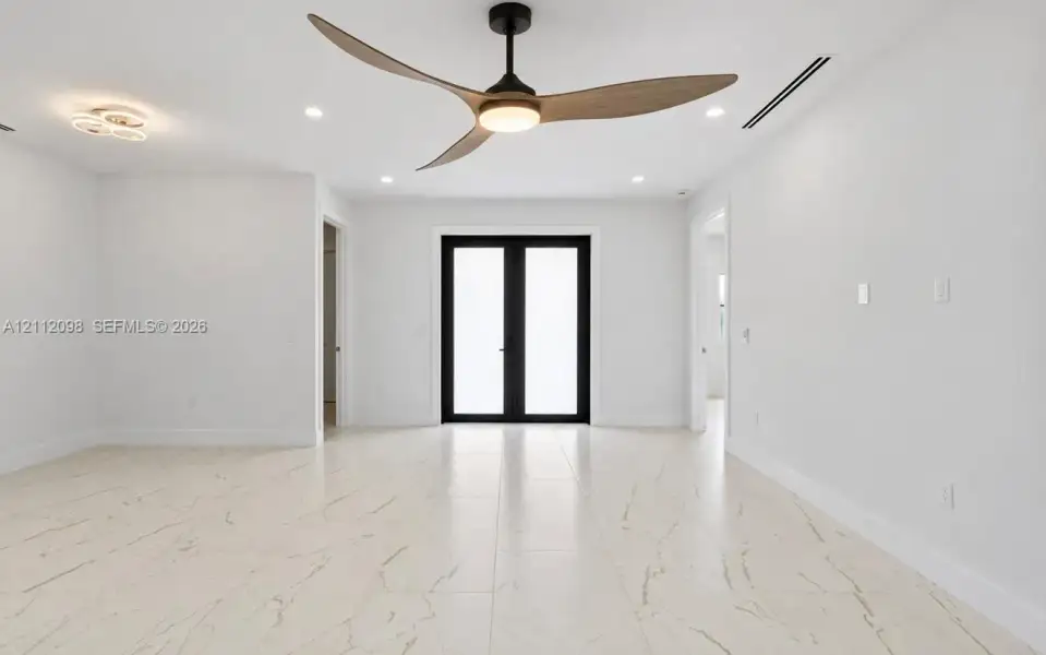 Spacious interior featuring large-format tile flooring with veining, three-blade ceiling fan with integrated lighting, dual glass-paneled exterior doors with black frames, and recessed lighting Spacious interior featuring large-format tile flooring with veining, three-blade ceiling fan with integrated lighting, dual glass-paneled exterior doors with black frames, and recessed lighting