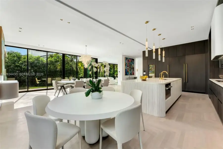 Open-concept kitchen featuring dark floor-to-ceiling cabinetry, a central island with a waterfall countertop, recessed ceiling lighting, multi-pendant illumination, and expansive floor-to-ceiling sliding glass walls