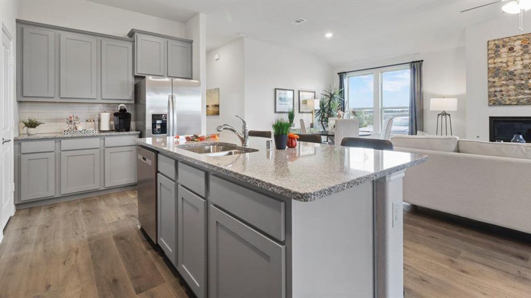 Kitchen featuring gray cabinets, open floor plan, a fireplace, stainless steel appliances, and light stone counters