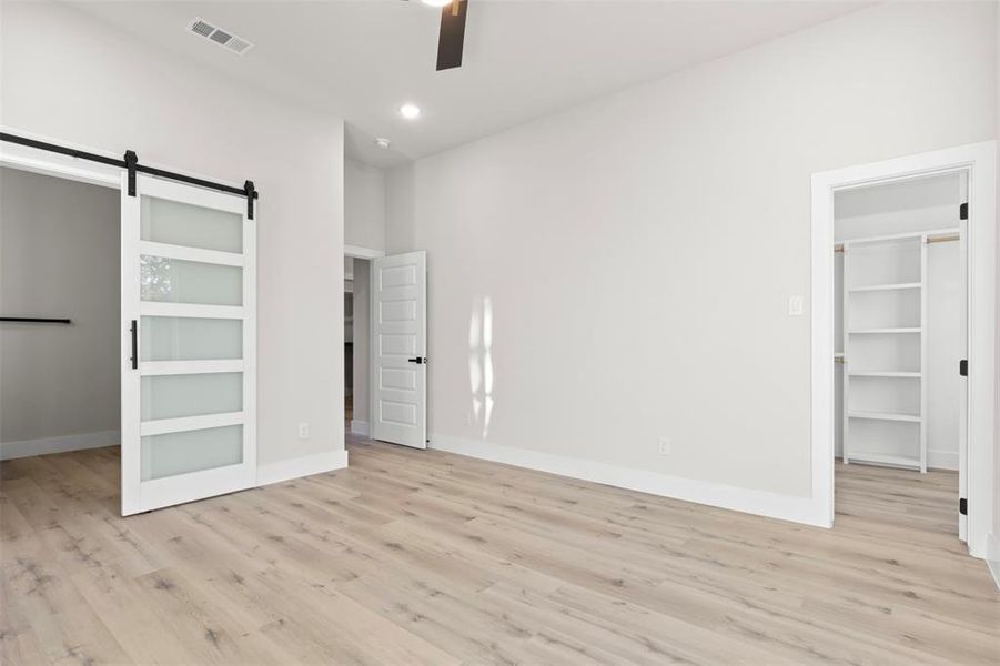 Unfurnished bedroom with ceiling fan, a barn door, light wood-type flooring, a spacious closet, and a closet