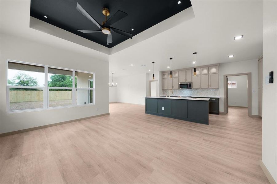 Kitchen featuring a sink, a raised ceiling, light wood-style flooring, stainless steel microwave, and open floor plan