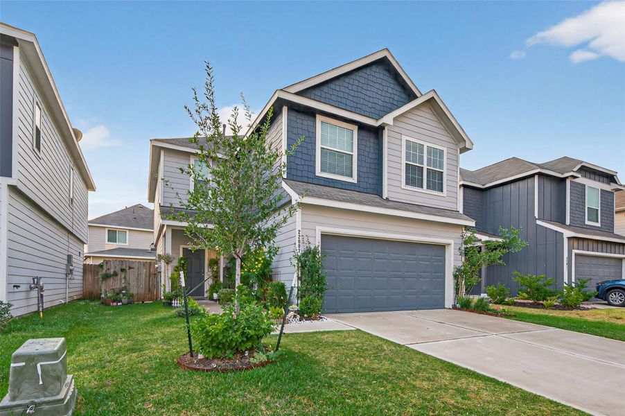 This is a modern two-story house with a gray and blue exterior, featuring a two-car garage and a well-maintained front yard. The property is part of a neighborhood with similar styled homes.