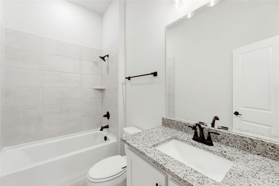 Bathroom with granite countertop vanity, white tub-shower combo with tile surround, and dark bronze fixtures