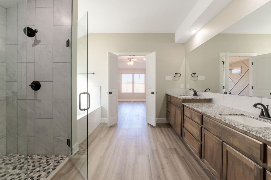 Full bathroom featuring a stall shower, double vanity, light wood finished floors, and a ceiling fan