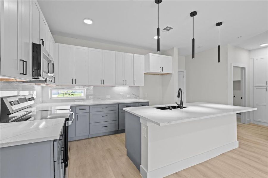 Kitchen with stainless steel appliances, light wood-type flooring, gray cabinetry, decorative light fixtures, and an island with sink