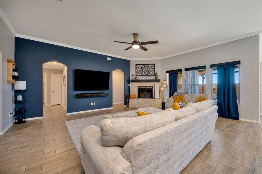 Living area with arched walkways, wood tiled floors, a fireplace, ceiling fan, and crown molding