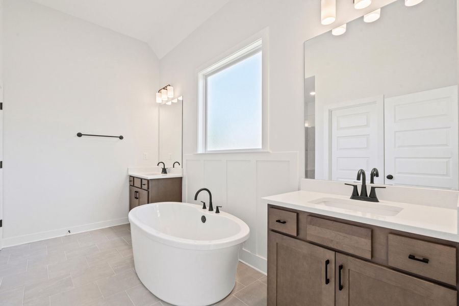 Freestanding soaking tub, dual vanities with white countertops, matte black plumbing fixtures, and tile flooring Freestanding soaking tub, dual vanities with white countertops, matte black plumbing fixtures, and tile flooring