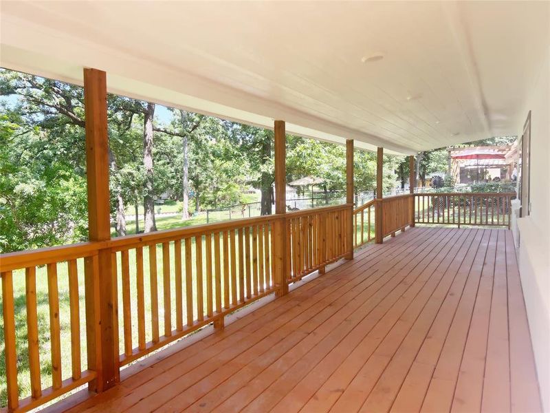 Expansive covered porch featuring wood decking, wood balusters and posts, a white plank ceiling, and recessed lighting