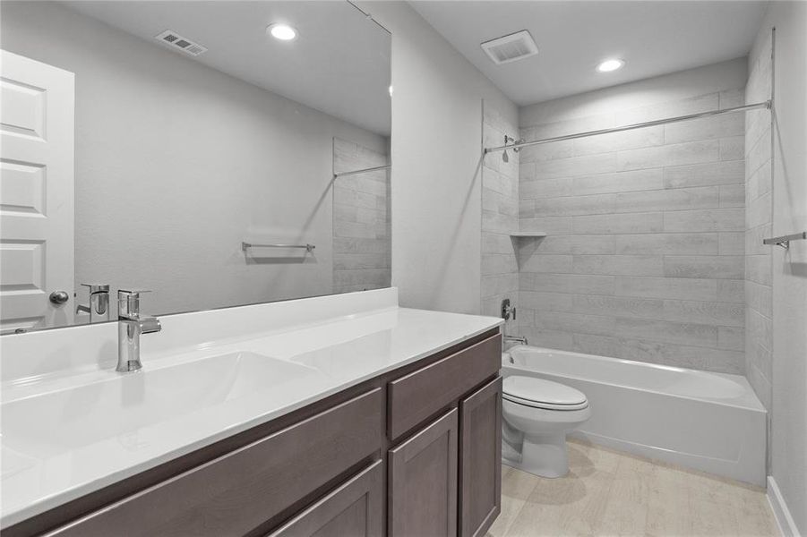 Secondary bath features tile flooring, bath/shower combo with tile surround, stained wood cabinets, beautiful light countertops, mirror, sleek fixtures and modern finishes.