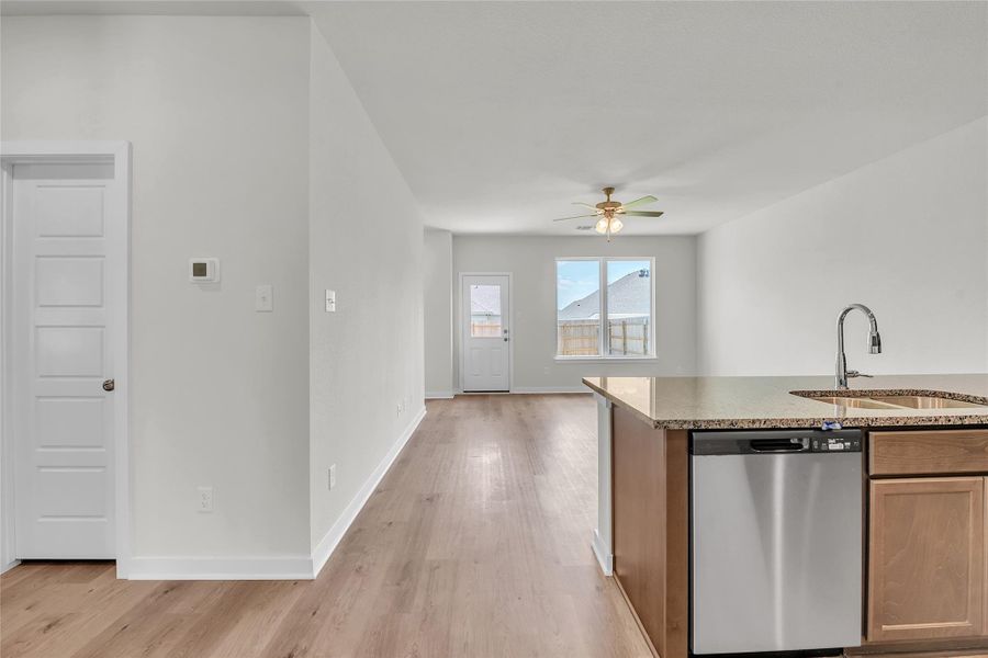 Kitchen with stainless steel dishwasher, light wood-style floors, light stone counters, and open floor plan Kitchen with stainless steel dishwasher, light wood-style floors, light stone counters, and open floor plan