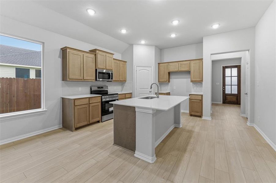 Kitchen featuring a central island with an undermount sink, light wood-finish cabinetry, stainless steel appliances, and wood-finish flooring
