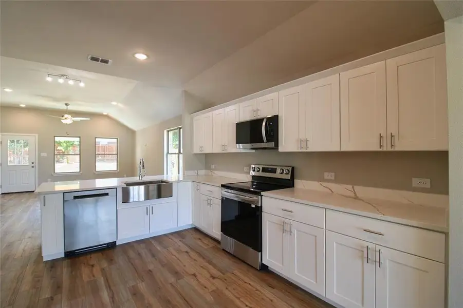 Kitchen featuring white cabinetry, appliances with stainless steel finishes, vaulted ceiling, dark wood finished floors, and recessed lighting