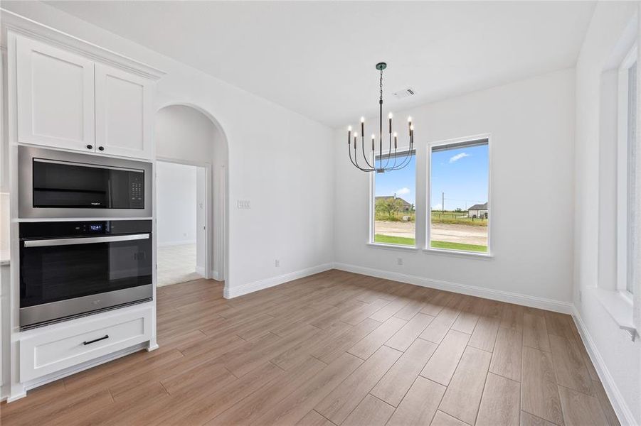 Kitchen featuring stainless steel appliances, a chandelier, arched walkways, light wood-style floors, and white cabinetry