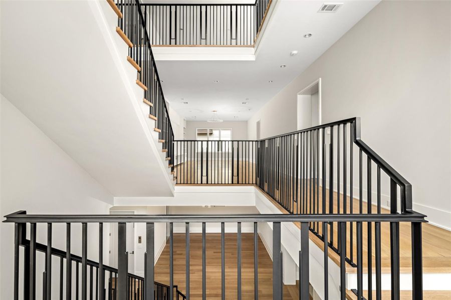 Dramatic open landing with sightlines across both levels, framed by modern iron railings.