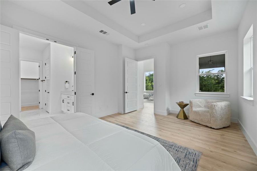 Bedroom with light wood-style floors, a tray ceiling, recessed lighting, ceiling fan, and ensuite bathroom Bedroom with light wood-style floors, a tray ceiling, recessed lighting, ceiling fan, and ensuite bathroom