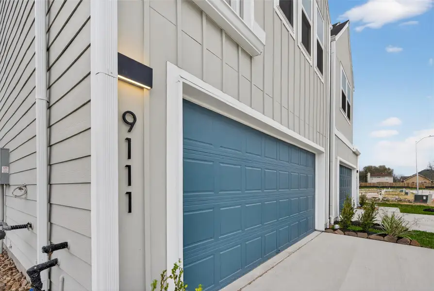 Contemporary garage design with a paneled blue finish, modern exterior lighting, and a vertical address feature that elevates the home’s exterior aesthetic. Contemporary garage design with a paneled blue finish, modern exterior lighting, and a vertical address feature that elevates the home’s exterior aesthetic.