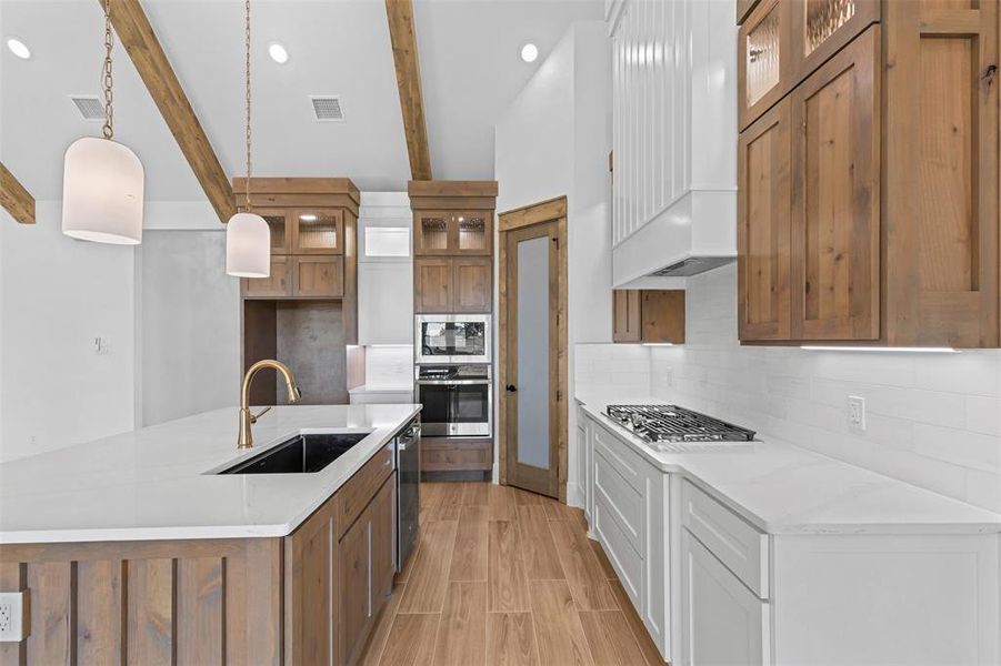 Kitchen with brown cabinets, pendant lighting, glass insert cabinets, tasteful backsplash, and a spacious island