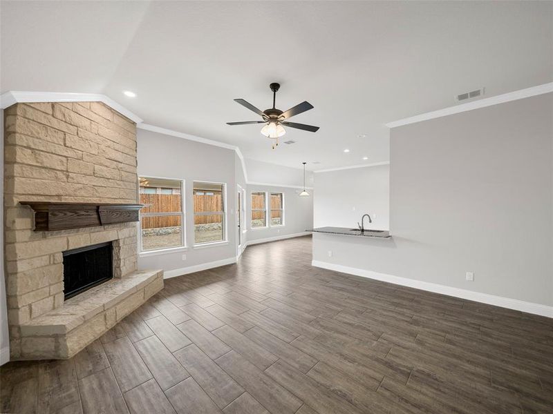 Unfurnished living room with dark wood finished floors, ceiling fan, a stone fireplace, and visible vents Unfurnished living room with dark wood finished floors, ceiling fan, a stone fireplace, and visible vents