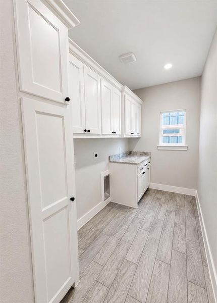 Utility room featuring extensive white shaker cabinetry, light-toned wood-finish flooring, a built-in counter with a stone-finish surface, recessed lighting, and a single window Utility room featuring extensive white shaker cabinetry, light-toned wood-finish flooring, a built-in counter with a stone-finish surface, recessed lighting, and a single window