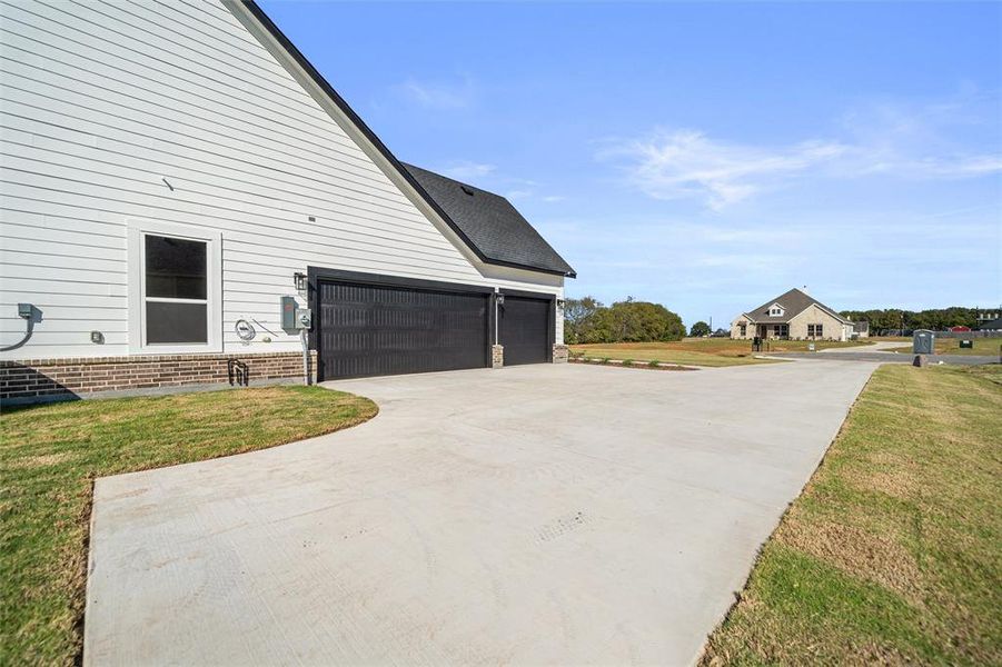 View of side of property featuring a lawn, a garage, driveway, and brick siding