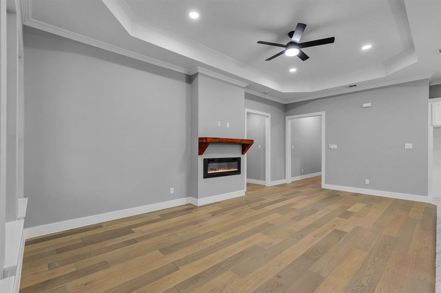 Unfurnished living room with ceiling fan, light wood-type flooring, crown molding, and a tray ceiling