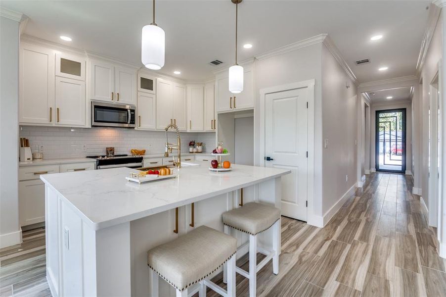 Kitchen featuring range with electric cooktop, tasteful backsplash, a kitchen island with sink, white cabinets, and crown molding