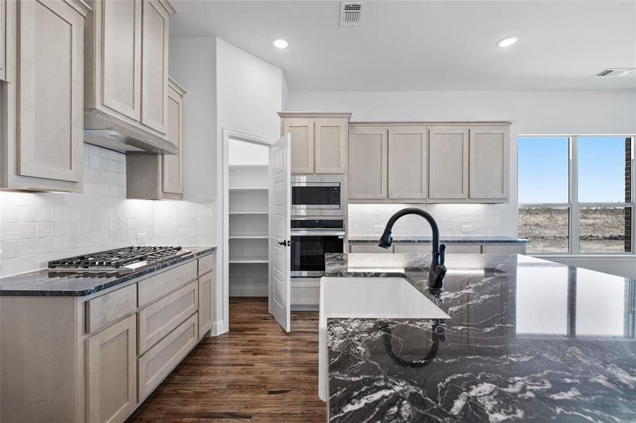 Kitchen with dark stone countertops, tasteful backsplash, dark wood-style floors, stainless steel appliances, and recessed lighting