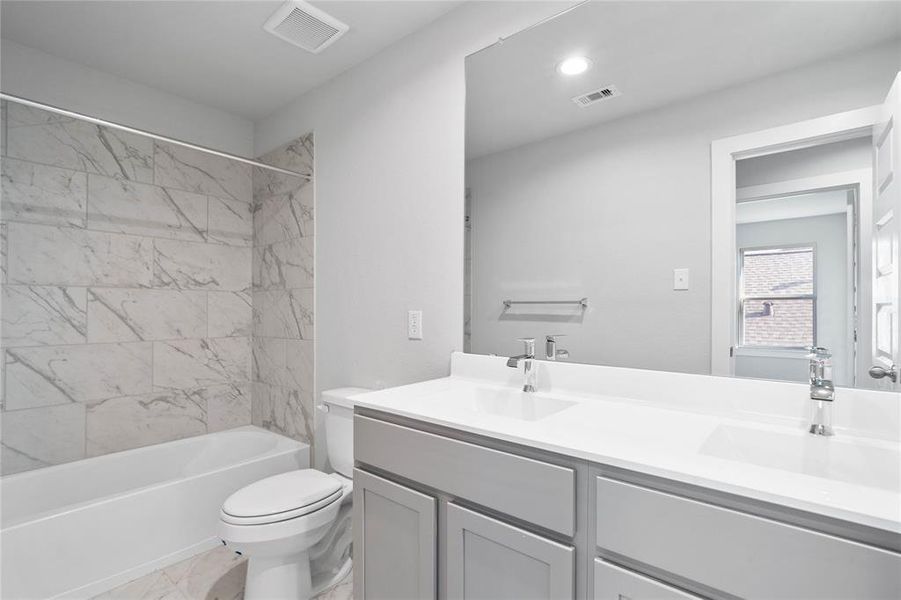 Secondary bath features tile flooring, bath/shower combo with tile surround, stained wood cabinets, beautiful light countertops, mirror, sleek fixtures and modern finishes.