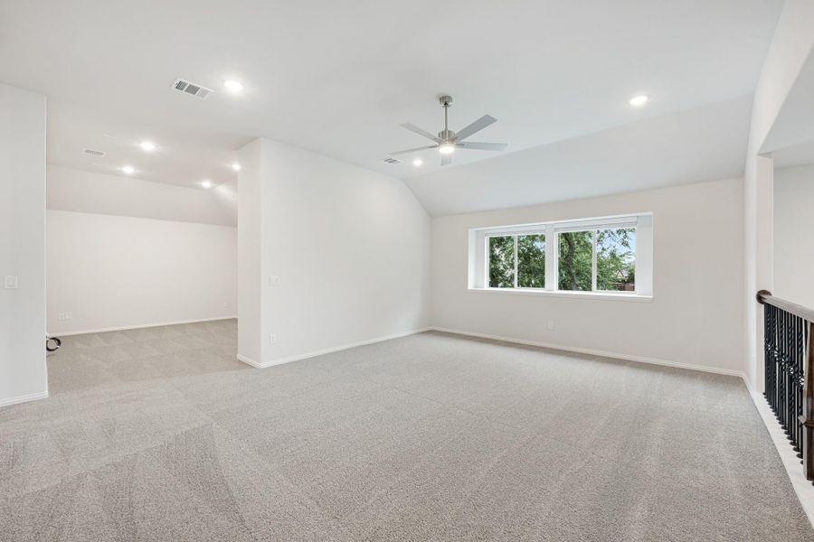 Large open bonus room with carpet, ceiling fan, vaulted ceiling, and staircase railing nearby Large open bonus room with carpet, ceiling fan, vaulted ceiling, and staircase railing nearby