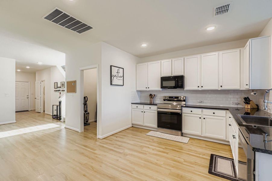 Kitchen featuring appliances with stainless steel finishes, tasteful backsplash, white cabinetry, recessed lighting, and light wood finished floors