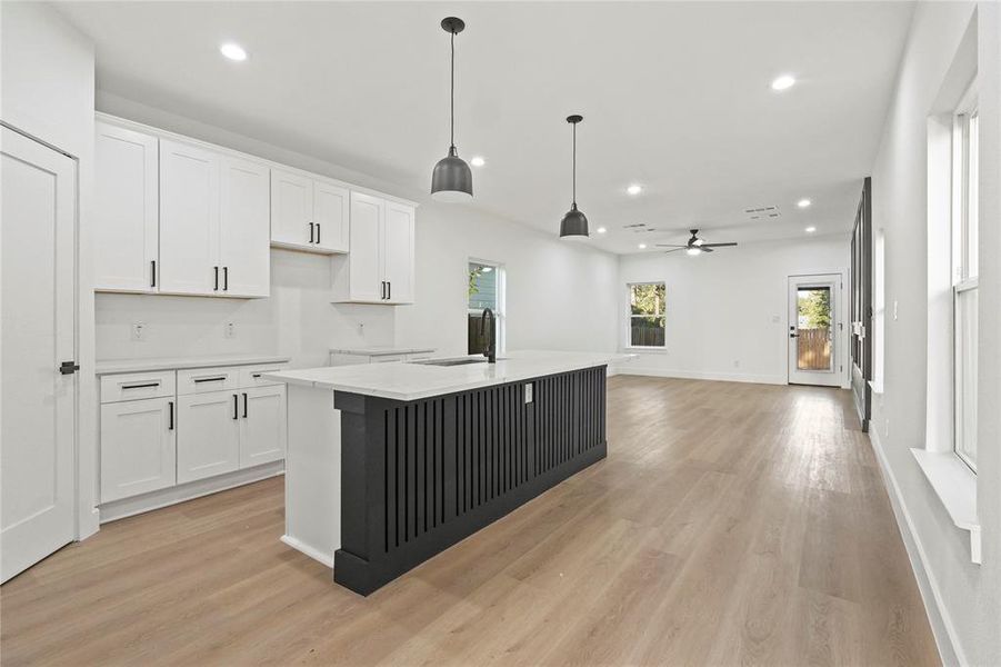 Kitchen with white cabinetry, recessed lighting, decorative light fixtures, a kitchen island with sink, and light stone countertops Kitchen with white cabinetry, recessed lighting, decorative light fixtures, a kitchen island with sink, and light stone countertops