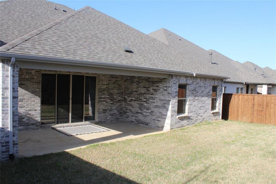 Rear view of house with a patio area, a lawn, fence, brick siding, and roof with shingles