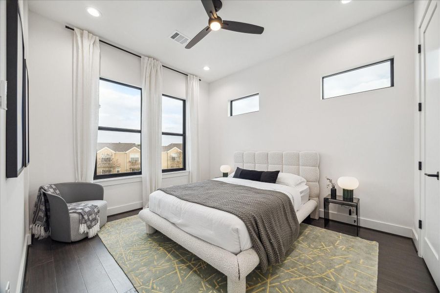 Light-filled secondary bedroom with large windows, high ceilings, and rich wide-plank flooring. Crisp white walls enhance the sense of openness, while the well-proportioned layout offers flexibility for guests or family members. A serene and inviting space that reflects the home’s consistent modern design throughout.