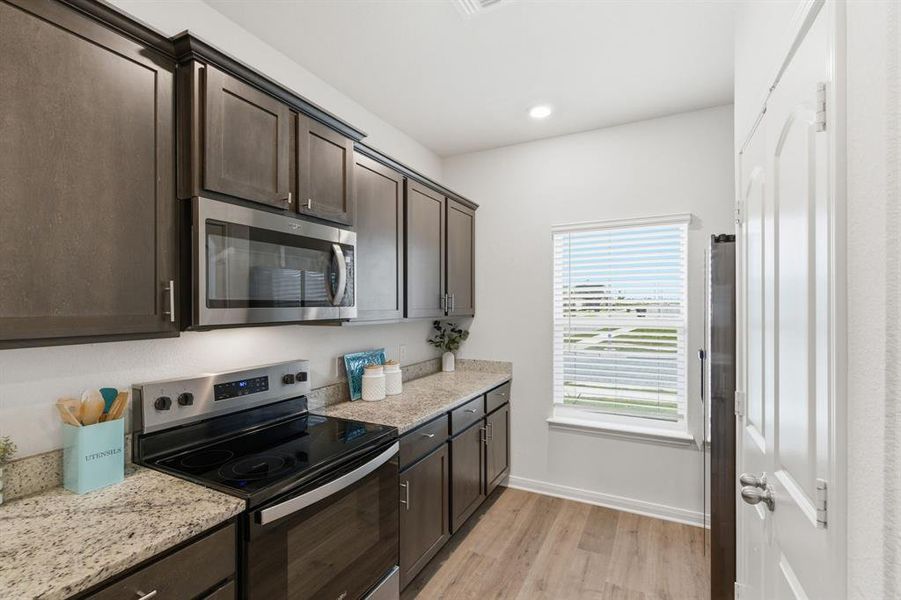 The kitchen features dark wood cabinetry, granite countertops, and stainless steel appliances including an oven with a stovetop and a microwave