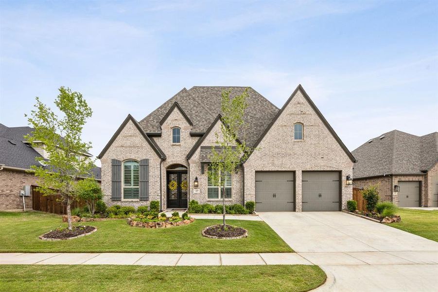 French provincial home featuring brick siding, driveway, a front yard, an attached garage, and roof with shingles
