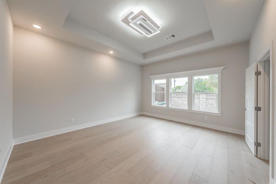 Unfurnished room with a tray ceiling, light wood-style flooring, recessed lighting, and cooling unit