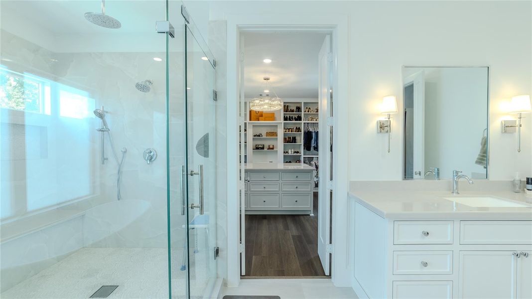 This photo showcases a modern bathroom with a spacious glass-enclosed shower, a sleek vanity with ample storage, and a well-lit mirror. The bathroom leads into a large walk-in closet with organized shelving and drawers, providing excellent storage solutions.