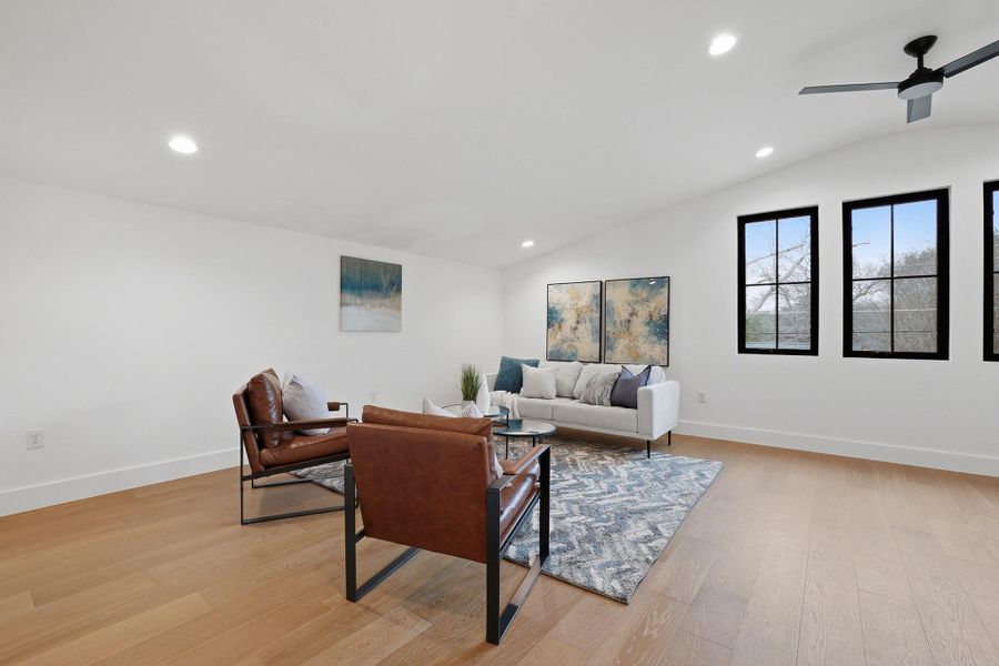 Spacious living area featuring light wood-finish flooring, recessed lighting, and a vaulted ceiling with a modern ceiling fan