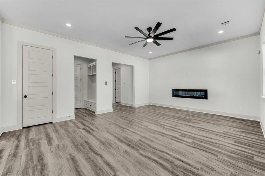 Unfurnished living room featuring crown molding, light wood finished floors, a glass covered fireplace, recessed lighting, and ceiling fan