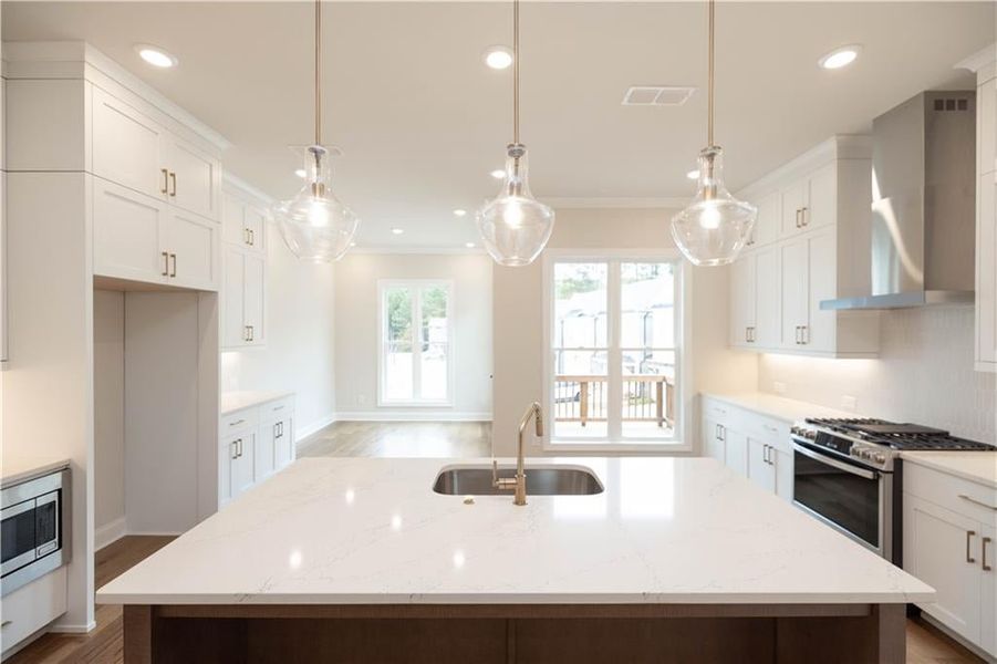 Kitchen featuring wall chimney range hood, sink, a kitchen island with sink, hanging light fixtures, and stainless steel appliances