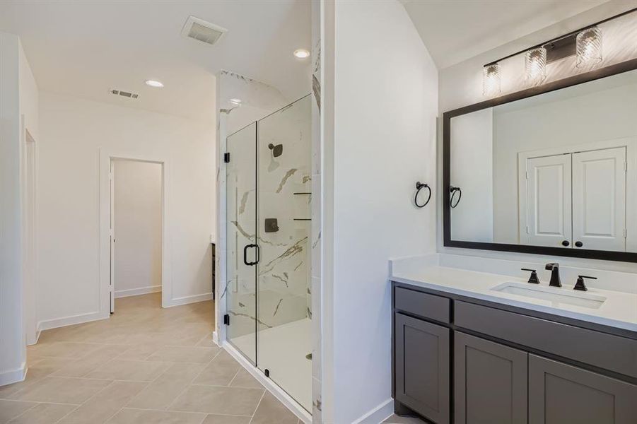 Bathroom with a marble finish shower, recessed lighting, vanity, and light tile patterned flooring