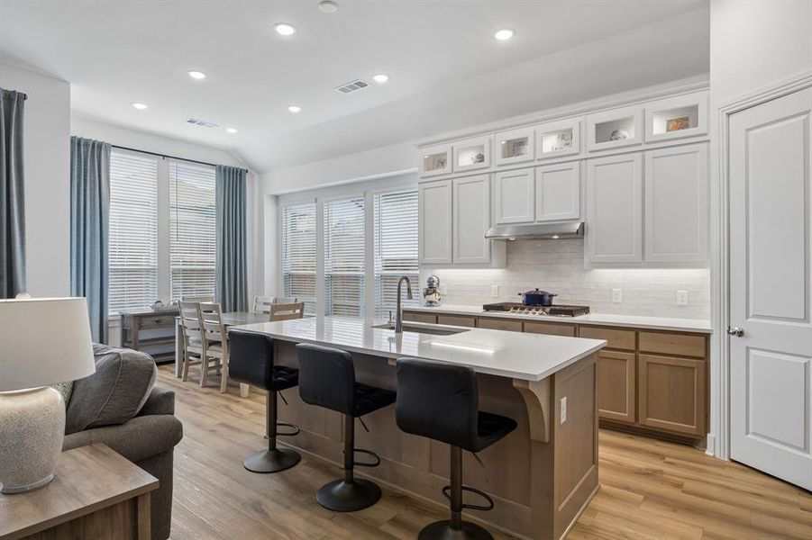 Open-concept kitchen featuring light-toned cabinetry, an island with seating, built-in cooktop, and wood-finish flooring