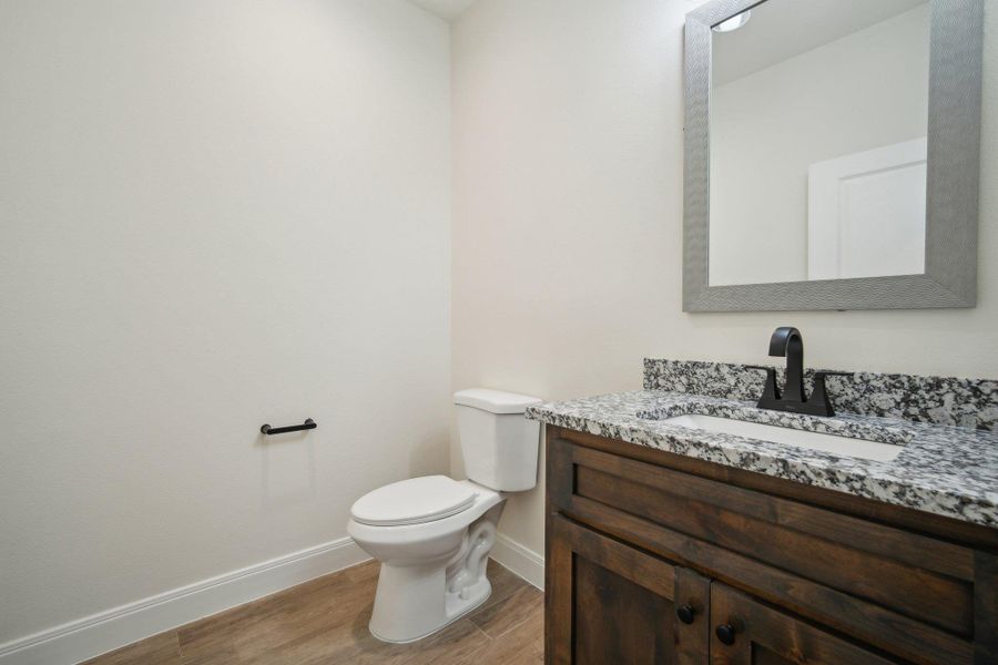 Half bathroom with baseboards, wood finished floors, toilet, and vanity Half bathroom with baseboards, wood finished floors, toilet, and vanity