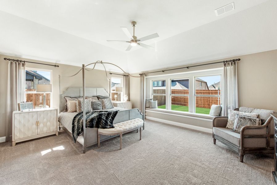 Spacious master bedroom with four-poster bed, ceiling fan, window seat, and neutral carpet